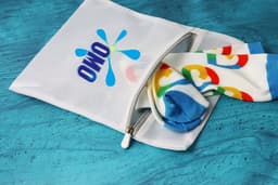 A white laundry bag with a logo, featuring colourful patterned socks peeking out from the zippered opening.