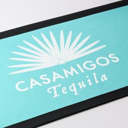 A turquoise bar runner featuring a palm leaf design and a logo, set against a black trim.
