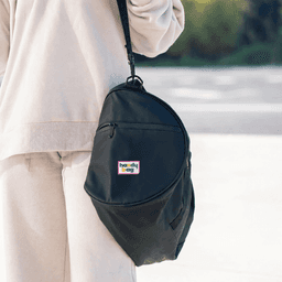 A black duffle bag with a logo, featuring a shoulder strap and zippered pocket, held by a person in light-coloured clothing.