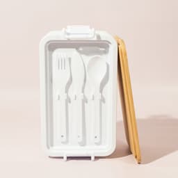 A white lunch box with a bamboo lid, featuring a fork, spoon, and knife inside. It has a simple, modern design.