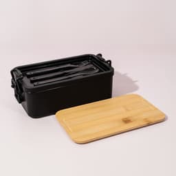 A black lunch box with a bamboo lid and utensils inside. It features a sleek design and a branded logo.