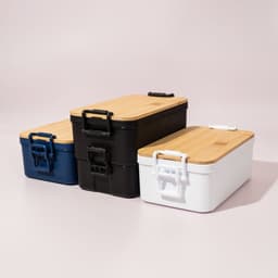 Three lunch boxes in navy blue, black, and white with bamboo lids and handles, displaying a sleek, modern design.