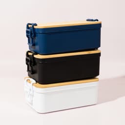 Three stacked lunch boxes in navy blue, black, and white, each with a wooden lid and a branded logo.