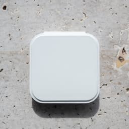 A white compact mirror with an LED light, featuring a square shape and a smooth surface, resting on a textured stone background.