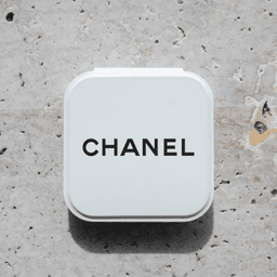 A compact mirror in a white case with a logo on the top, set against a textured stone background.