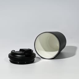 A travel cup in black with a removable lid, featuring a stainless steel inner lining and a sleek design.