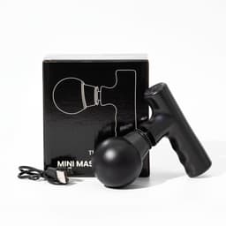 A black mini massage gun beside its box and a charging cable, featuring a sleek design and rounded head.