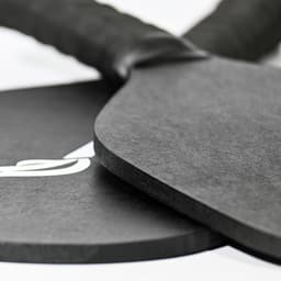 A black pickleball paddle and ball set with a textured grip, featuring a logo on one item.