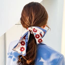 A silk satin scarf featuring a floral pattern in red and blue, tied in a bow in a woman's hair.