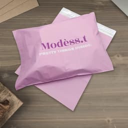 A purple biodegradable mailer bag with a white seal and a logo, resting on a wooden surface.