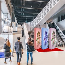A pink and blue straight fabric popup display stands in a modern exhibition space with stairs and escalators in view.