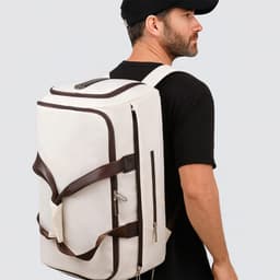 A white convertible backpack duffel garment bag with brown straps, displayed on a person wearing a black cap and shirt.