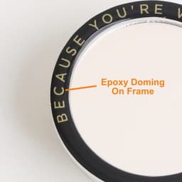 A custom-shaped mirror phone pop holder with a black frame and an epoxy domed finish. It features a logo on the edge.