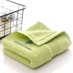 A folded green embroidered cotton hand towel displayed next to a wire basket. The towel features a logo.