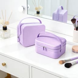 Two lavender portable mini suitcases are placed on a vanity, alongside makeup brushes and a decorative vase.