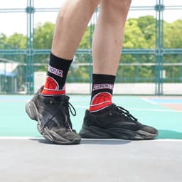 Crew sport socks featuring a basketball design in red and black, worn with black athletic shoes on a sports court.