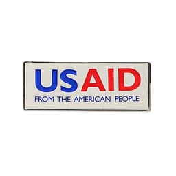 A rectangular lapel pin in blue, red, and white colours featuring a logo and text.