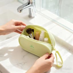 A round, light green silicone storage bag holds various cosmetic items and brushes on a marble countertop.