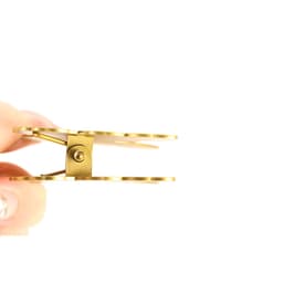 A custom metal clip with a shiny gold finish, held between fingers, showcasing its design and hinge mechanism.