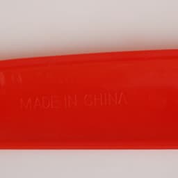 A bright red V Shaped Boomerang Toy with a smooth surface and a faint imprint indicating its place of manufacture.