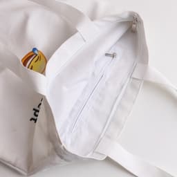 A white velvet tote bag with a zip pocket inside and dual handles. It features a logo design.