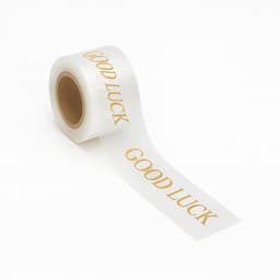 A roll of clear ribbon featuring the phrase "Good Luck" in gold lettering. The ribbon is glossy and stretches out from the roll.