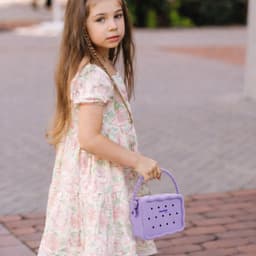 A purple silicone bag with holes, being carried by a girl wearing a floral dress in an outdoor setting.