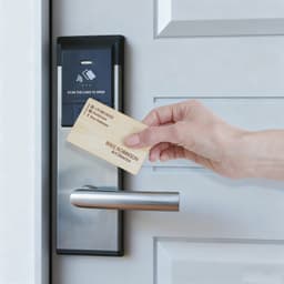 A bamboo business card is being held near a contactless door lock with a sleek silver handle.