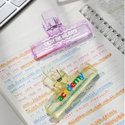 Translucent plastic clips in purple and yellow resting on handwritten notes, with a notebook and a computer keyboard in the background.