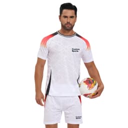 A man wearing a white crew neck tee shirt with red and black accents, holding a soccer ball. The shirt has a logo.