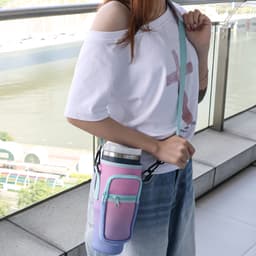 A drink bottle carrier bag in pink and purple, featuring a phone pocket, worn over the shoulder by a person.