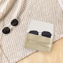 A PU leather glasses pouch in gold, holding a pair of dark sunglasses, set on a textured fabric background.