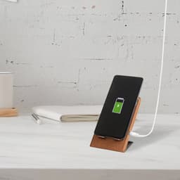 A wireless charger with a cork stand and a smartphone displaying a charging icon, set on a minimalist desk.