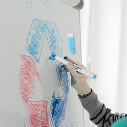 A blue magnetic whiteboard marker in use, with a gloved hand drawing on a whiteboard featuring colourful designs.