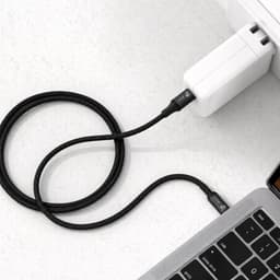 A black braided charging cable connected to a white power adapter and a laptop. It features a logo on the cable.