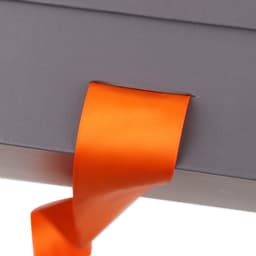 A small grey foldable box with a vibrant orange ribbon peeking out from its side, featuring a logo.