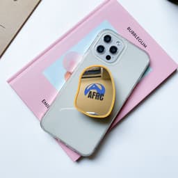 A yellow custom-shaped mirror phone pop holder on a clear phone case, resting on a pink book.