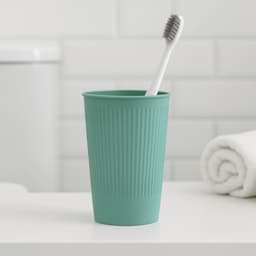 A teal wheat straw toothbrush cup with ridged texture, containing a white toothbrush, set on a bathroom counter.
