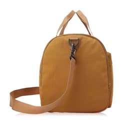 A foldable travel duffle bag in a warm mustard colour with a sturdy strap and top handles. Features a hook closure and branding.