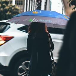 An expandable golf umbrella in shades of blue, held by a person, featuring a logo and geometric designs.