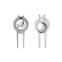 A silver golfers divot tool featuring a round ball marker with a logo. The tool has a pronged design for easy use.