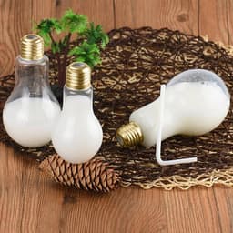A drink bottle in the shape of a light bulb, featuring a clear body and gold lid, accompanied by two others on a rustic mat.