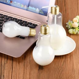 A drink bottle shaped like a light bulb, clear with a gold lid, featuring a straw and a smooth white liquid.