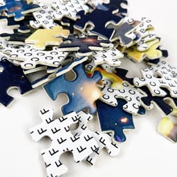 A pile of jigsaw puzzle pieces featuring a cosmic design in blue, yellow, and black hues, with some pieces showing a grid pattern.