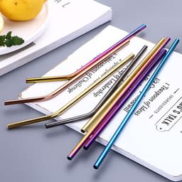 A set of stainless steel drinking straws in various metallic colours, arranged on a flat surface with some plates beside them.