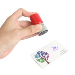 A round stamp with a red top and grey base held above a business card featuring a colourful tree design.