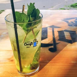 A tall glass tumbler filled with a minty green drink, garnished with fresh mint leaves and a straw.