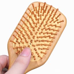 A bamboo hair brush featuring wooden pins and a natural finish, held in a hand.