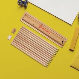 A set of 12 wooden coloured pencils with a ruler and sharpener, arranged on a yellow background.