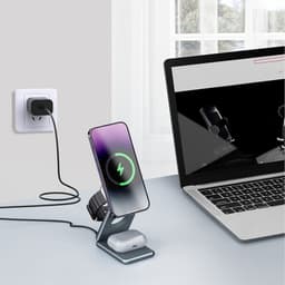 A foldable wireless charger stand in grey, charging a phone and earbuds, placed next to a laptop.